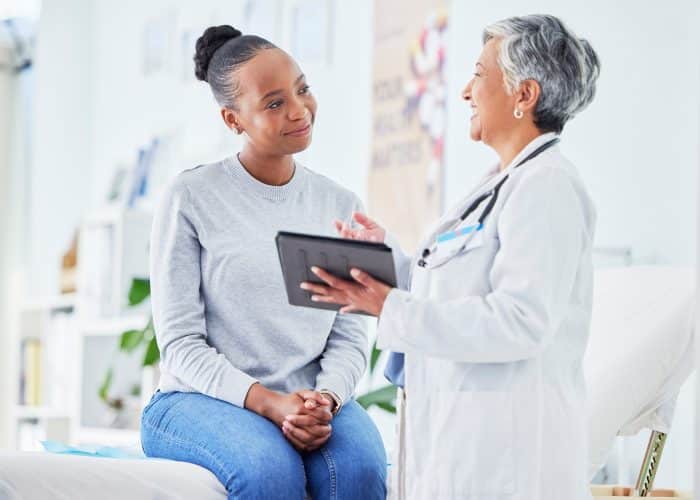 Doctor, women and tablet for happy healthcare, hospital news and support with test results or exam on bed. Senior nurse and patient with digital registration, clinic sign up and medical consultation